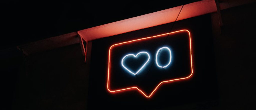 Photograph of neon sign with Instagram symbol for likes. A zero is next to the heart. Image via Unsplash