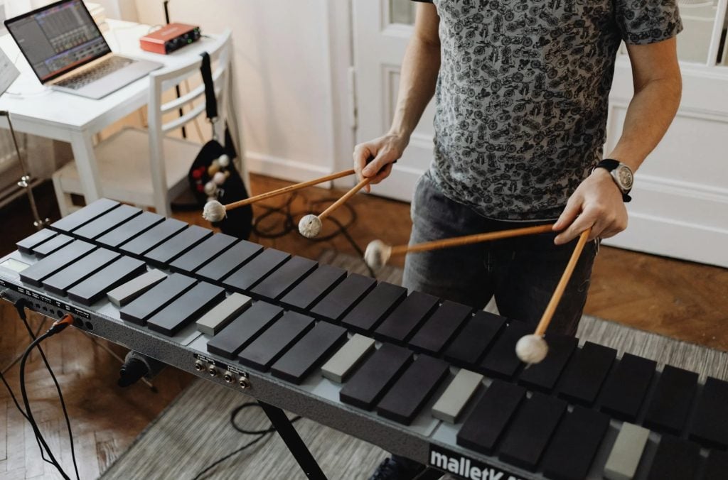 A music advertising appeal depicted by a person from the chest down playing a xylophone indoors.