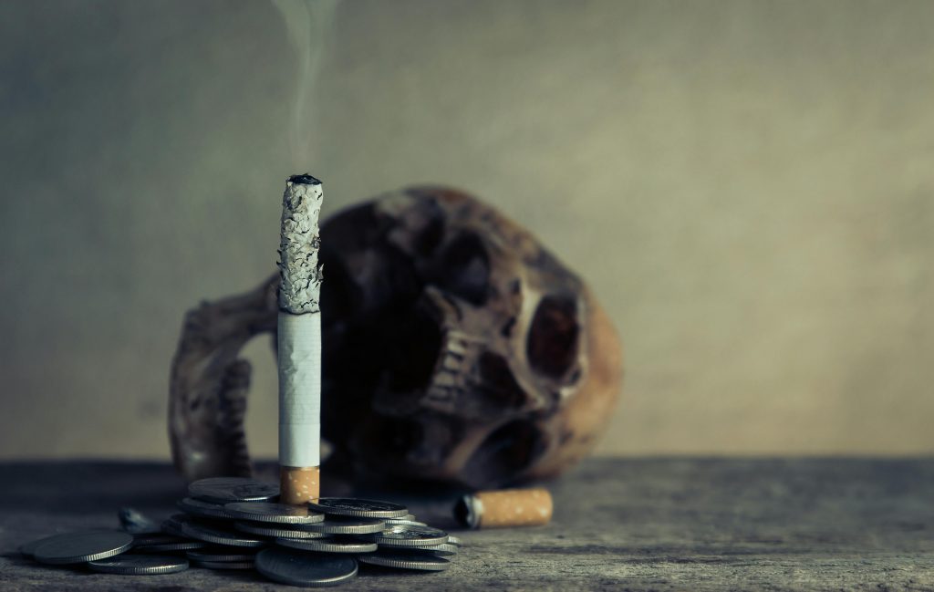 A fear advertising appeal of a cigarette burning atop a pile of coins with a skull in the background.