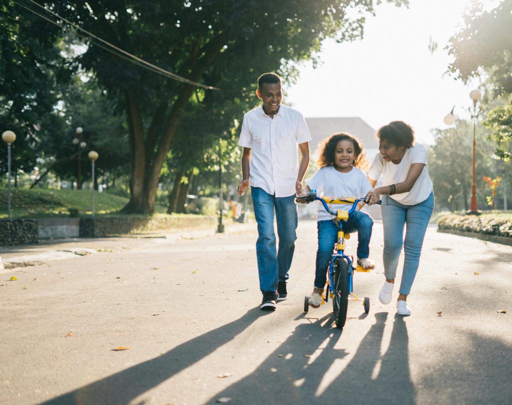 Emotional advertising appeal depicting a family of three with a little kid learning to ride a bike along a quiet street during the day.