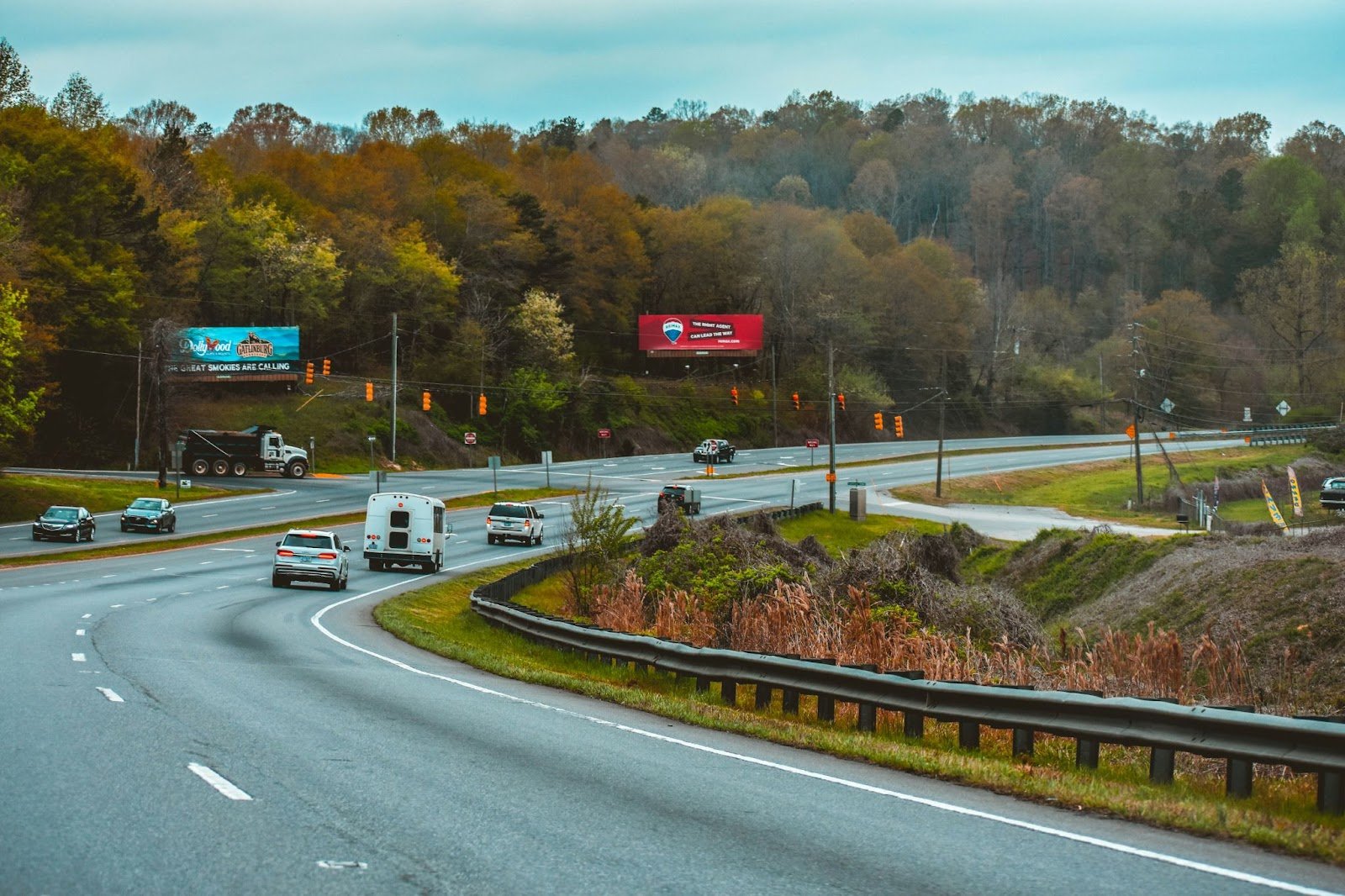 Photo of a curved highway with vehicles and two billboards among trees