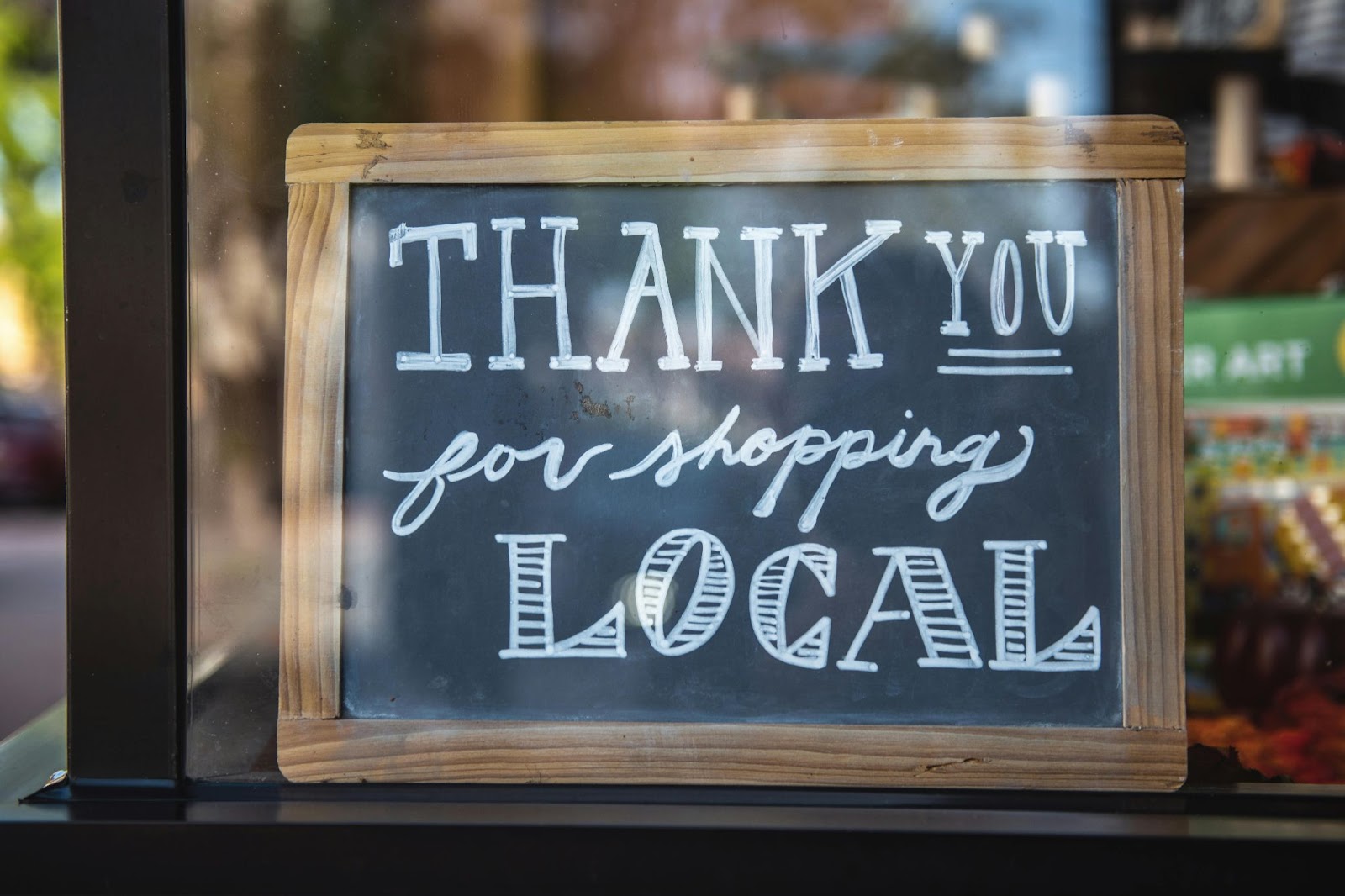 small chalkboard sign seen through a window that reads: thank you for shopping local